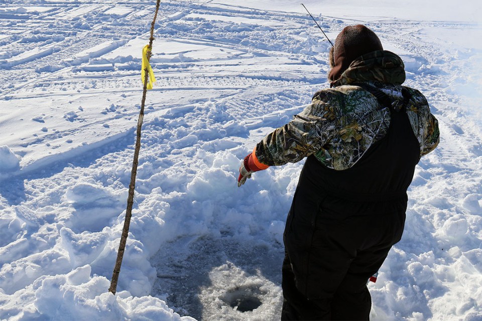 Man stands over a small hole in the ice with a fishing pole.