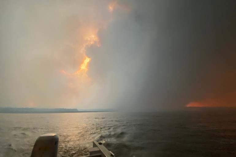 Smoke fills the air as evacuees leave Fort Simpson by boat on the evening of June 29, 2026. Photo: Dawn Isaiah