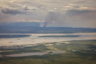 A wildfire burns in the distance across the Mackenzie River from Norman Wells on June 15, 2026. Ollie Williams/Cabin Radio