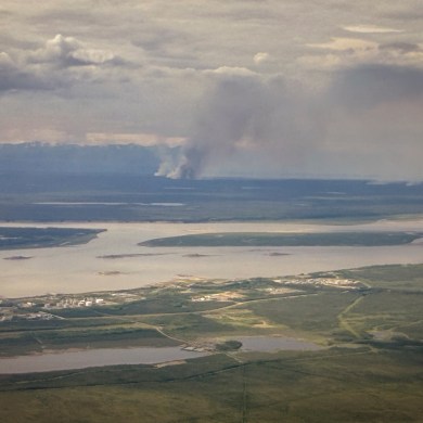 A wildfire burns in the distance across the Mackenzie River from Norman Wells on June 15, 2026. Ollie Williams/Cabin Radio