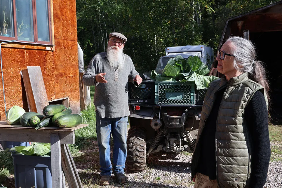 A man and a woman stand next to large produce. The man is gesturing as he speaks.
